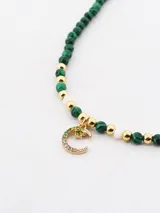 Collar corto de cuentas facetadas color verde esmeralda y detalles dorados. Dije de luna creciente con incrustaciones de strass. Cierre de mosquetón.
