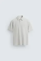 Polo gris claro de piqué con cuello solapa, cierre frontal de botonadura y manga corta.