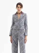 Chaqueta corta (cropped) con estampado a cuadros gris y azul claro, cuello solapa de cuero color bordó y bordados a juego. Presenta bolsillos con tapa en el frente y mangas con puños acampanados.
