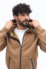 Campera de felpa color camel con cierre frontal, capucha ajustable con cordones negros y bolsillos laterales con cierre negro. Presenta un estampado pequeño en el pecho con texto en color oscuro.