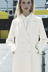 Abrigo largo color crudo de Zara Woman Collection, con cuello solapa, manga larga, bolsillos de vivo con solapa y cierre frontal cruzado con botones.