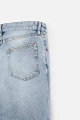 Pantalón de jean negro con efecto lavado, corte flare, cinco bolsillos, cierre frontal con cremallera y botón, y bajo con acabado irregular.
