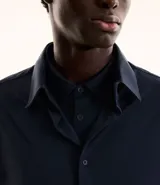 Camisa azul marino de manga larga, confeccionada en tejido piqué de poliamida y elastano. Cuenta con cuello inglés, abotonadura frontal y tecnología performance que ofrece elasticidad, secado rápido y resistencia a las arrugas.