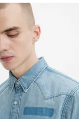 Camisa de denim celeste de corte recto, con mangas largas, cuello clásico, cierre con botones a presión, dos bolsillos con solapa abotonada en el pecho y canesú en la espalda.