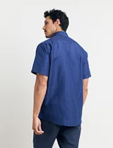 Camisa de manga corta azul con pequeños lunares blancos, cuello abotonado y bolsillo en el pecho.