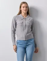 Cardigan color beige en tejido jacquard, con cuello con solapa y abertura central con cierre. Delantera con bolsillos simulados.