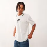 Camiseta tipo polo de manga corta, color blanco, confeccionada en tejido de malla perforada. Presenta cuello con ribete negro y logo "Nike Air" estampado en el pecho en color negro.