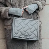 Cartera tipo tote color gris con diseño acolchado en símil cuero. Tiene acceso con cierre, asas fijas y correa regulable extraíble. El interior está forrado en tela de algodón y poliéster y cuenta con un bolsillo con cierre y dos abiertos.