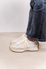 Zapatillas deportivas color beige con detalles metalizados dorados, perforaciones, cordones ajustables y suela de goma dentada.