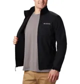 Chaqueta softshell Columbia para hombre, color negro, con cierre frontal, cuello alto y logo de la marca en blanco en el pecho. Presenta bolsillos laterales y uno en el pecho con cierre.