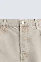 Pantalón de jean color beige, de corte amplio y tiro alto, con cinco bolsillos, efecto lavado y cierre frontal con botones.