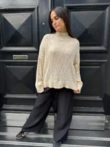 Sweater color crema de punto trenzado, con cuello alto y mangas largas.