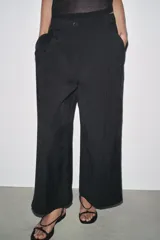 Pantalón cropped marrón de tiro medio y pierna ancha, confeccionado en hilatura con mezcla de lyocell. Presenta trabillas en la cintura, bolsillos laterales y pinzas en el delantero. Cierre frontal con cremallera y botón.