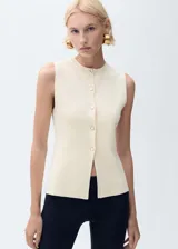 Chaleco de punto fino color crema, con cuello redondo, sin mangas y cierre frontal con botones.