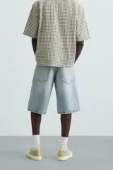 Bermuda de denim de algodón, color gris claro lavado, de corte ancho (baggy fit) y largo hasta la rodilla. Presenta cinco bolsillos y cierre frontal con cremallera y botón.