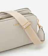 Bolso bandolera mediano color marrón, con correa ancha de tela con rayas beige y blancas. Tiene tres compartimentos con cierre de cremallera y detalles metálicos dorados.