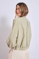 Cazadora color verde oliva con cuello redondo, cierre frontal con botones y mangas largas con puños elásticos.