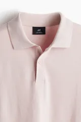 Chomba de piqué de algodón color rosado, de corte clásico, con cuello clásico, tapeta de botones y mangas cortas con terminación acanalada.