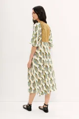 Vestido midi color crudo con estampado floral en tonos celeste y ocre, escote en V con detalle bordado y mangas cortas amplias.