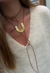 Collar con dije de herradura dorada y cordón de cuero sintético marrón.