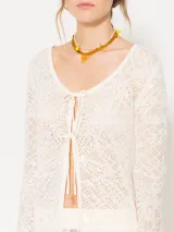 Cárdigan de tejido calado color crema con lentejuelas, de silueta liviana y femenina. Presenta escote redondo y cierre frontal con lazos finos.