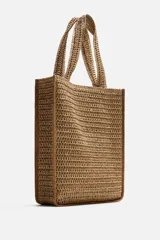 Bolso tipo shopper color marrón claro, con acabado trenzado. Tiene un compartimento principal con cierre de imán y un bolsillo plano interior. Cuenta con dos asas de mano.