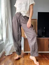 Pantalón de lino color marrón topo, de corte amplio, con cintura elastizada ajustable con cordón, bolsillos laterales y un bolsillo tipo cargo en la pierna derecha.