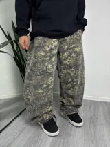 Pantalón baggy de camuflaje con estampado de hojas y ramas en tonos verde, marrón y gris.