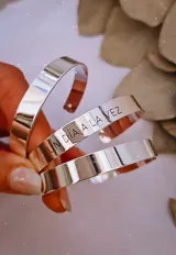 Brazalete rígido de metal plateado con frase grabada.