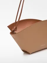 Bolso de hombro de cuero color beige y negro, con forma geométrica asimétrica y asa fina negra.