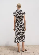 Vestido midi de manga corta con cuello camisero y cierre de botones frontal. Presenta un estampado floral grande en blanco y negro, y un cinturón ajustable a juego.