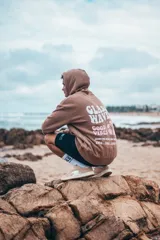 Buzo hoodie marrón con capucha y cordones ajustables. Estampado en la espalda con la frase "Glassy Waves", "Good Vibes", una flor y las fechas "1971, 1982, 1993".