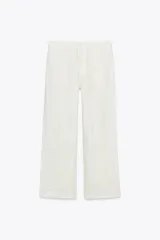 Pantalón blanco de lino con tiro medio, cintura ajustable con cordones, bolsillos laterales ocultos y detalle de entredós combinados a tono.