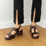 Sandalias de cuero vacuno color marrón con textura tipo cocodrilo, taco ancho y plataforma. Diseño con puntera descubierta y tira ancha sobre el empeine con aberturas laterales. Cierre con hebilla en el tobillo.