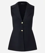 Chaleco negro de tejido punto, sin mangas, con cuello solapa y cierre frontal de dos botones dorados. El corte es acinturado y alargado.