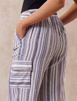Pantalón de lino a rayas verticales en tonos beige, azul y blanco. Tiene pretina elastizada, bolsillos inclinados delanteros y bolsillo lateral tipo cargo.