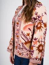 Chaqueta color crema con bordados florales en tonos tierra, rojizos y morados.