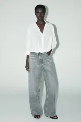 Camisa blanca de cuello solapa y manga larga con puños. Tiene un nudo en la parte delantera y cierre frontal con botones.