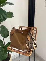 Bolso marrón de tela con correa larga al hombro y pañuelo estampado con animal print atado a una de las asas.