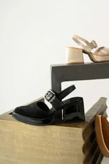 Zapatos de charol negro con tacón cuadrado y cierre ajustable en la parte posterior.
