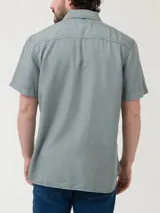 Camisa de manga corta color verde grisáceo, con cuello clásico, cierre frontal con botones de madera y bolsillo de parche en el pecho. Presenta bordado de un pato al tono en el bolsillo y pinza en la espalda para un ajuste moderno. Confeccionada en tejido de tencel.