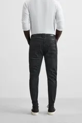 Pantalón de jean negro con corte skinny fit, cinco bolsillos, lavado con efecto roto y cierre frontal con cremallera y botón.
