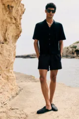 Short de baño negro de tela con tajos laterales cortos, elástico en la cintura con cordón ajustable, bolsillos laterales y bolsillo trasero con cierre autoadherente. Suspensor interior de malla.