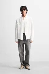 Sobrecamisa verde militar de lino, corte relaxed fit, con cuello solapa, manga larga con puños abotonados, bolsillos de parche con solapa en el pecho, aberturas laterales en el bajo y cierre frontal abotonado.