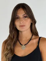 Gargantilla con cuentas de piedra negra y dije plateado en forma de sol.