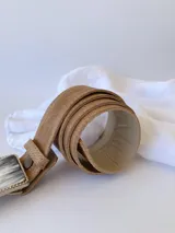 Cinto de cuero color marrón con forro de cuero y hebilla rectangular con diseño de guampa en blanco y negro con marco metálico plateado.