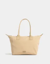 Bolso tipo shopper color beige con doble asa corta de hombro, cierre superior y tag de goma con logo.