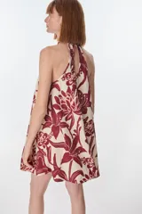 Vestido corto con estampado floral en tonos rojo y beige, cuello halter y corte evasé.