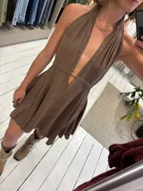 Vestido corto color marrón, con escote halter profundo en V y cintura marcada. La falda es acampanada y con vuelo.