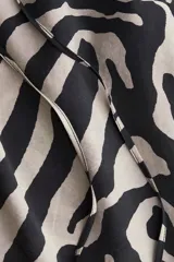 Blusa oversized de tejido liviano con estampado de cebra en tonos beige y negro. Tiene escote en V con cordón ajustable, mangas globo al codo de corte raglán y puños elásticos.